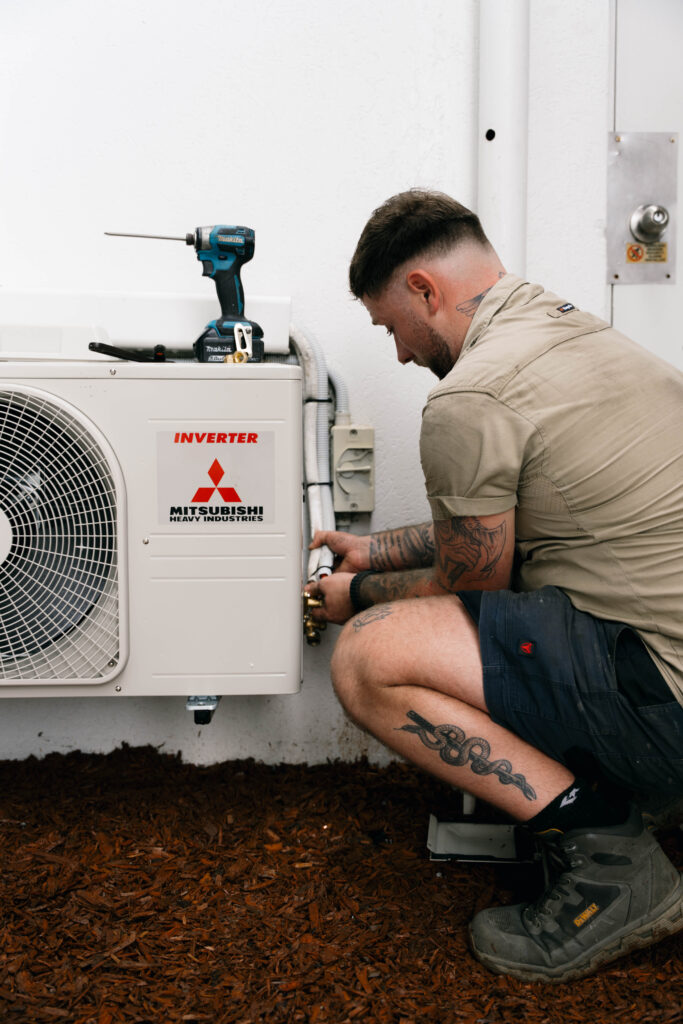 Technician kneeling beside an outdoor air conditioning condenser unit during a residential install