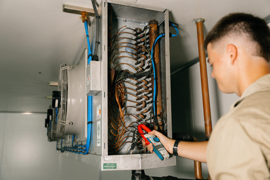 Technician working inside an open refrigeration control panel and copper pipework