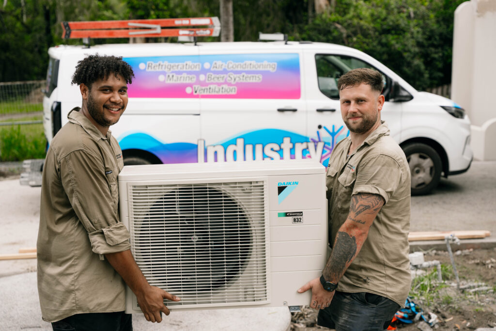 Two technicians unloading an outdoor condenser unit from a branded service van