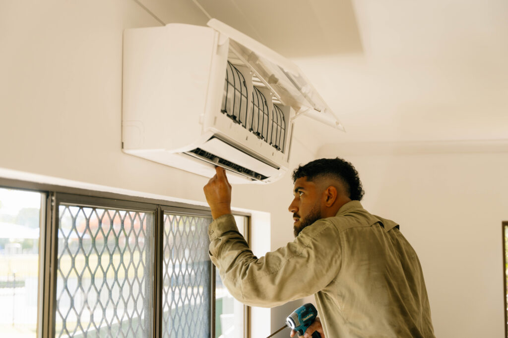 Two technicians fitting a wall-mounted split system air conditioner indoors