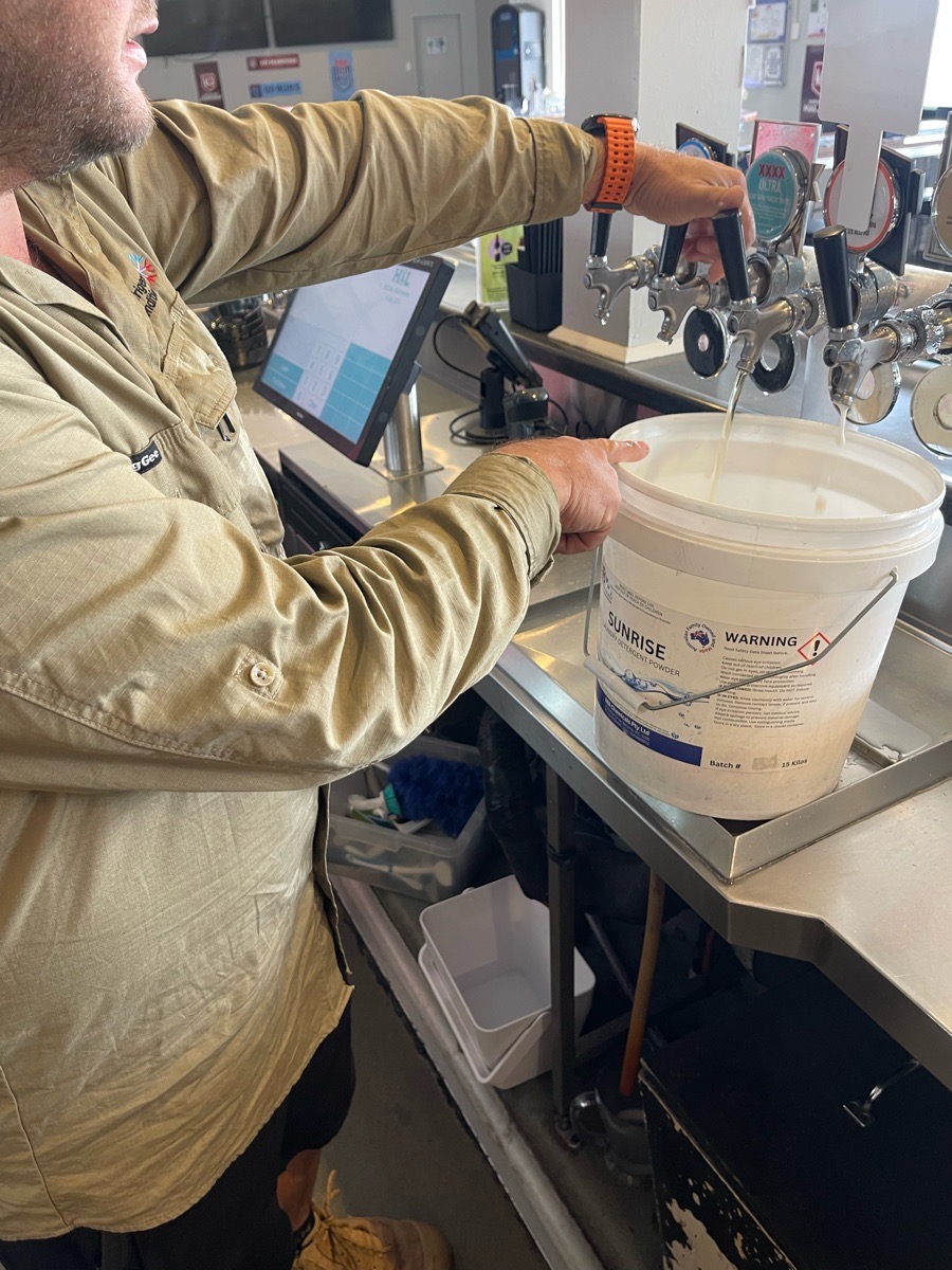 Technician holding a flush bucket beneath commercial beer taps